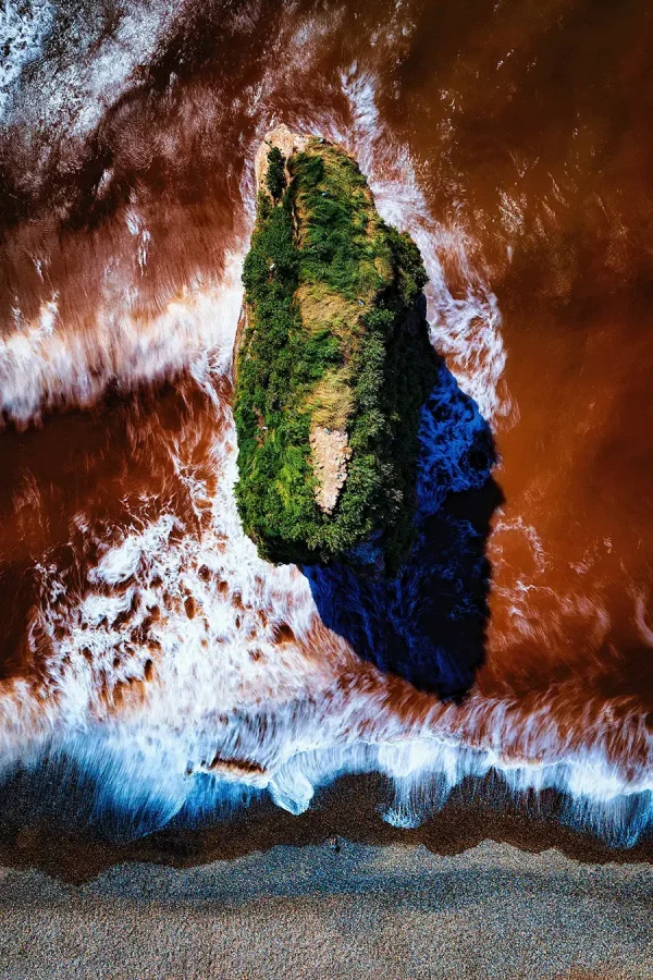 aerial view of Tavin coastline with waves going over orange sand and cliff